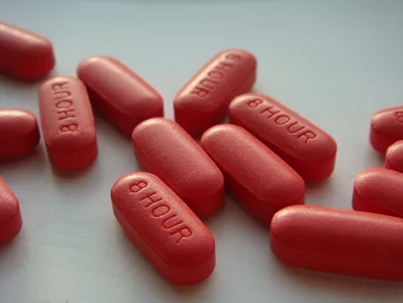 A close-up photograph of several red, capsule-shaped pills scattered on a white surface, each embossed with the text '8 HOUR'.