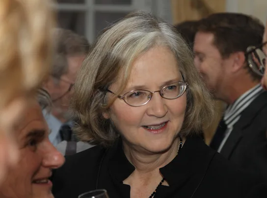 Elizabeth Blackburn, an older woman with shoulder-length gray hair and glasses, smiling at a reception, with blurred guests in the background.