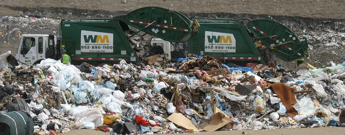 Photo shows two garbage trucks dumping their contents into a landfill.